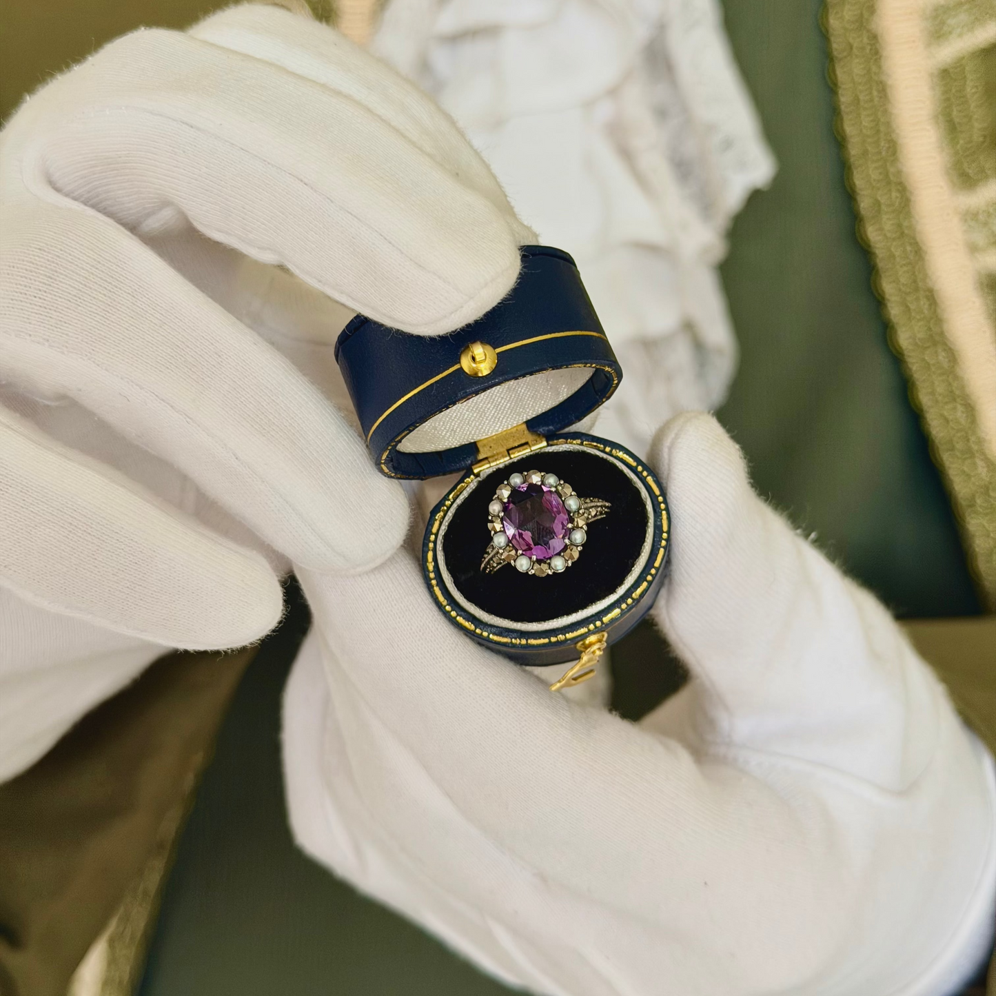 Brilliance amethyst and seed pearl halo ring in 925 silver in a navy antique ring box held by white-gloved hands