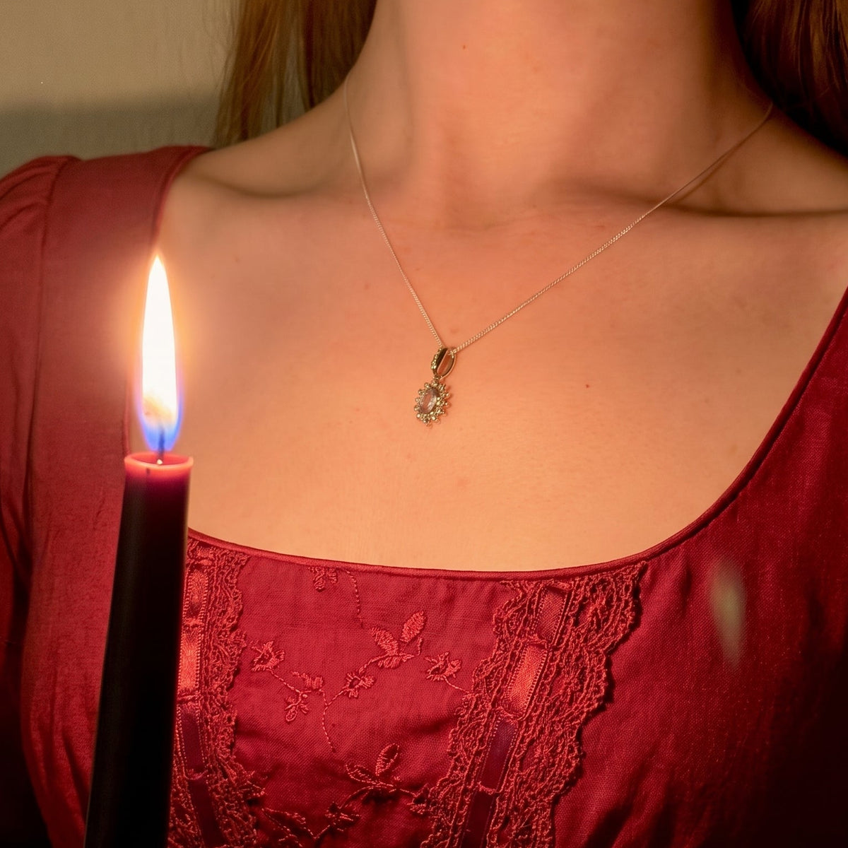 Woman in a red Regency-style dress wearing the blue topaz and pearl Cosmos pendant necklace by candlelight