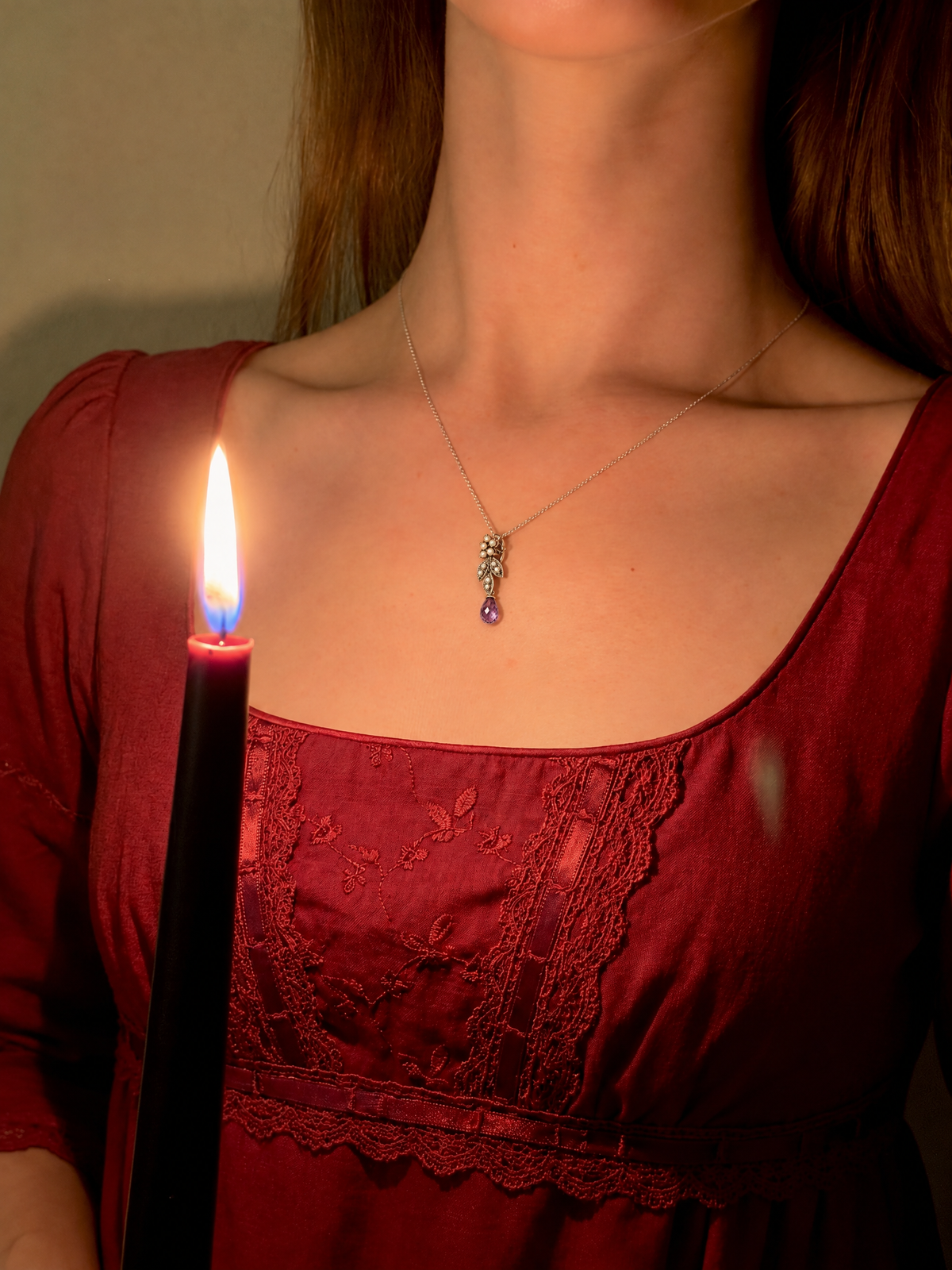 Woman in a red Regency-style dress wearing the Old Roots amethyst and pearl silver pendant by candlelight