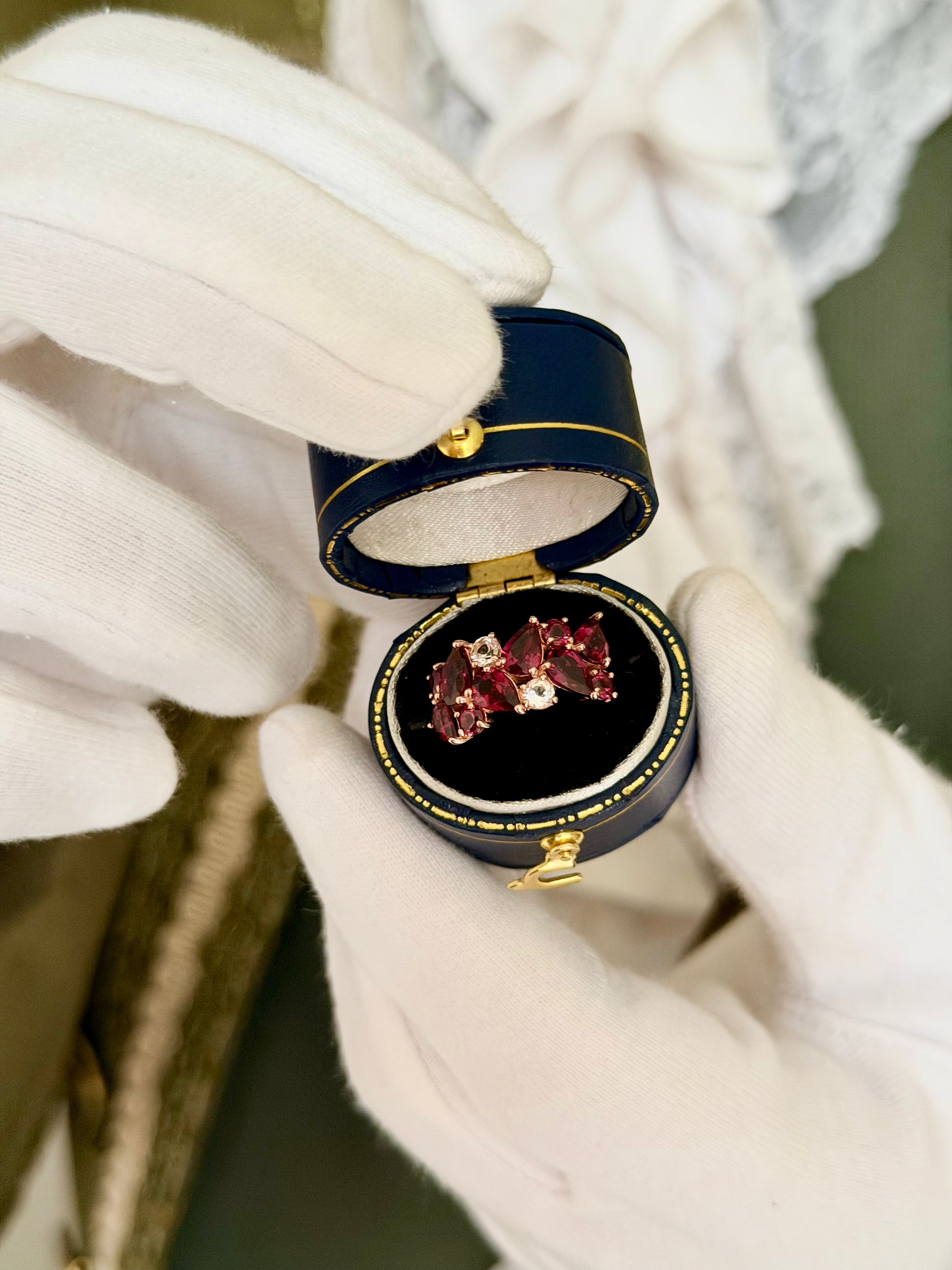 Berries in Gold purple rhodolite garnet ring in a navy antique ring box held by white-gloved hands