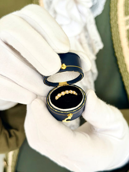 Gold plated Daisy Chain pearl ring in a navy antique ring box held by white-gloved hands