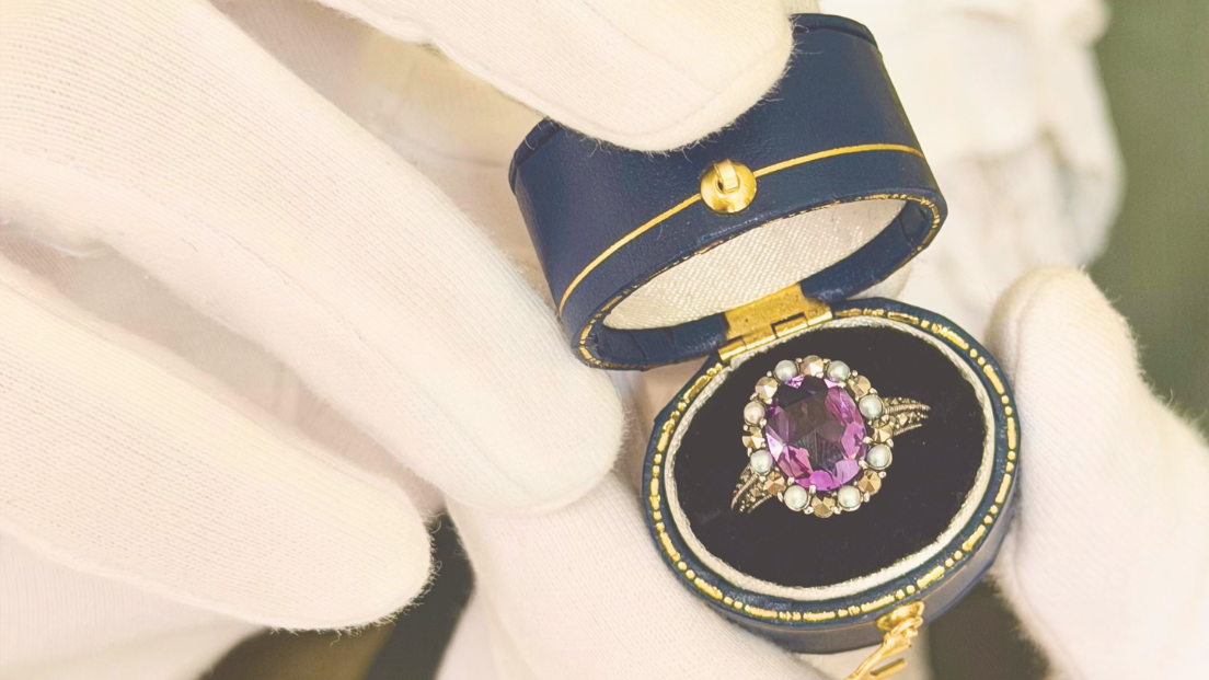 Duke Proposal Brilliance Ring, a vintage-style purple gemstone and pearl halo ring in an antique navy ring box