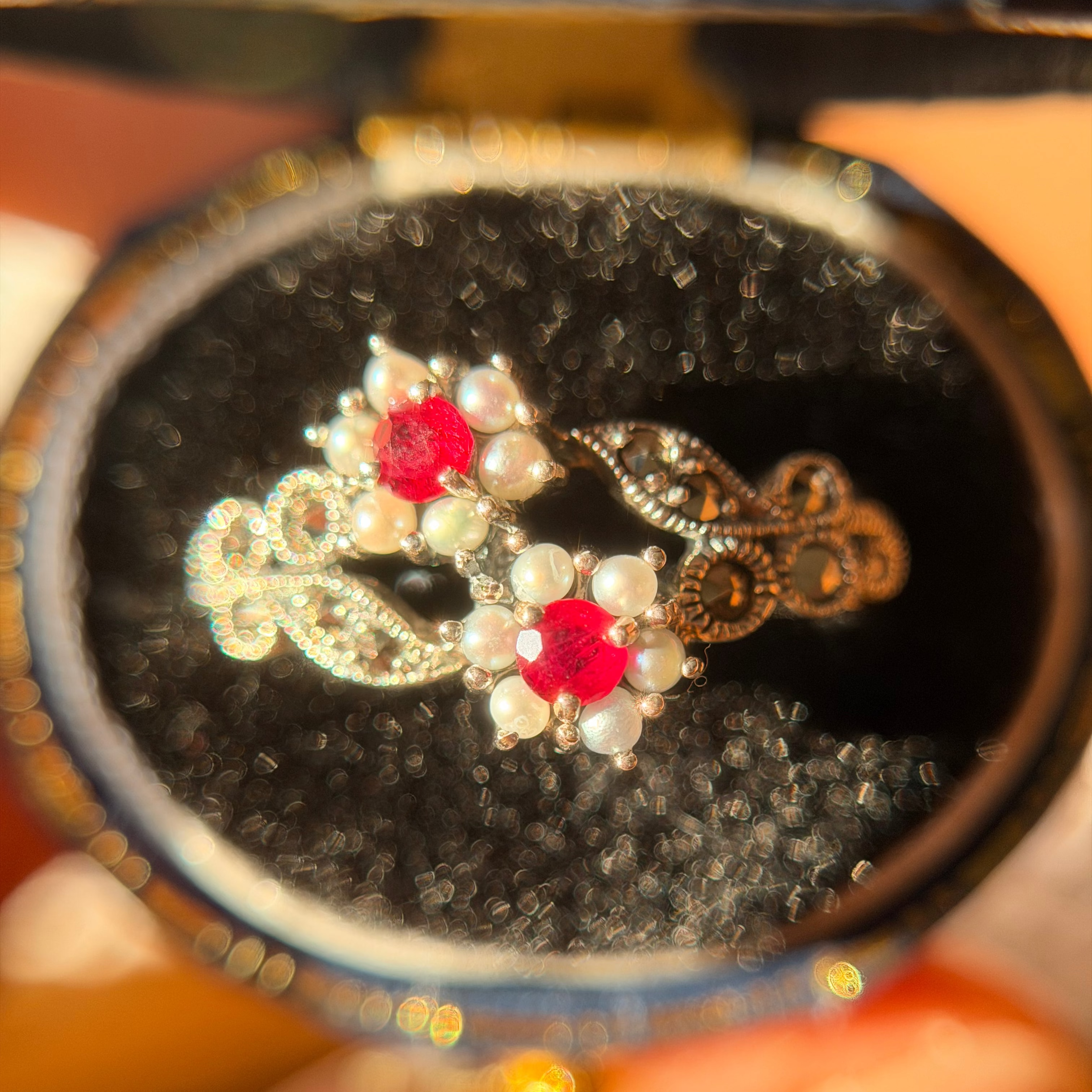 Close-up of vintage-style 925 silver ring with red gemstones, pearls and marcasite in an antique ring box