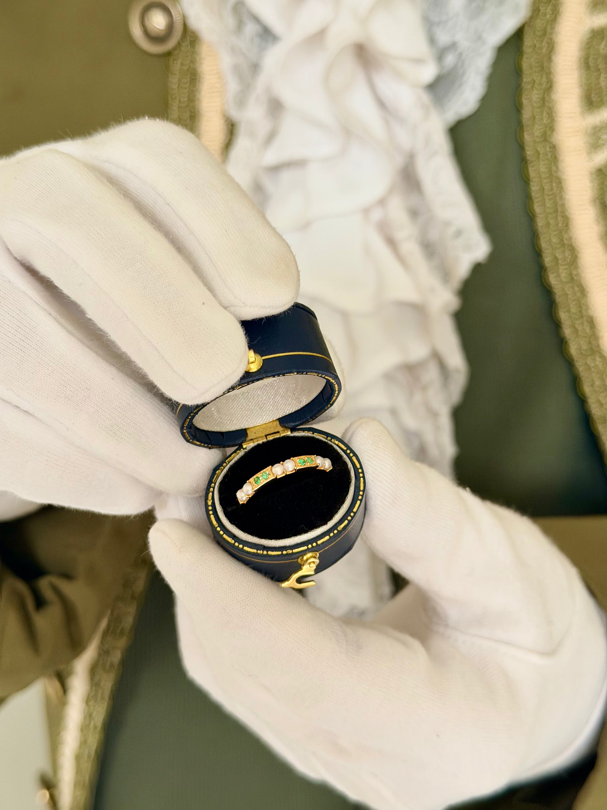 Gold plated Emerald Gaze emerald and pearl eternity ring in a navy antique ring box held by white-gloved hands