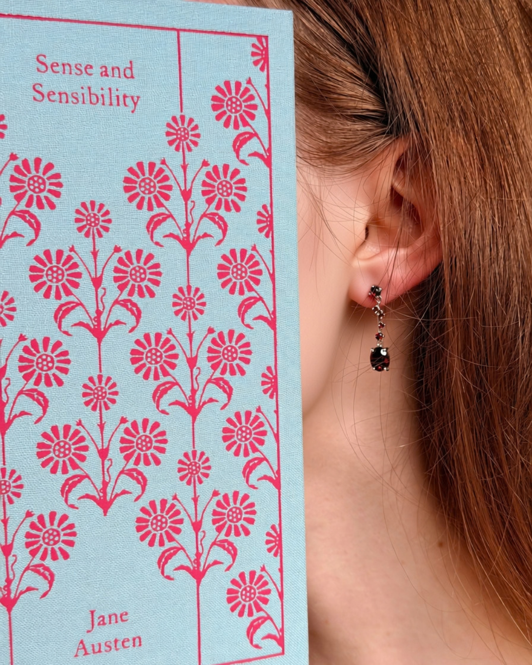 Model wearing silver Garnets on the Vine garnet drop earrings beside a Jane Austen book, vintage-inspired jewellery