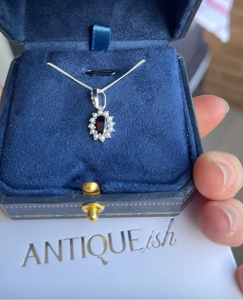 Customer photo of the Cosmos Pendant in Garnet, presented in a ring box.